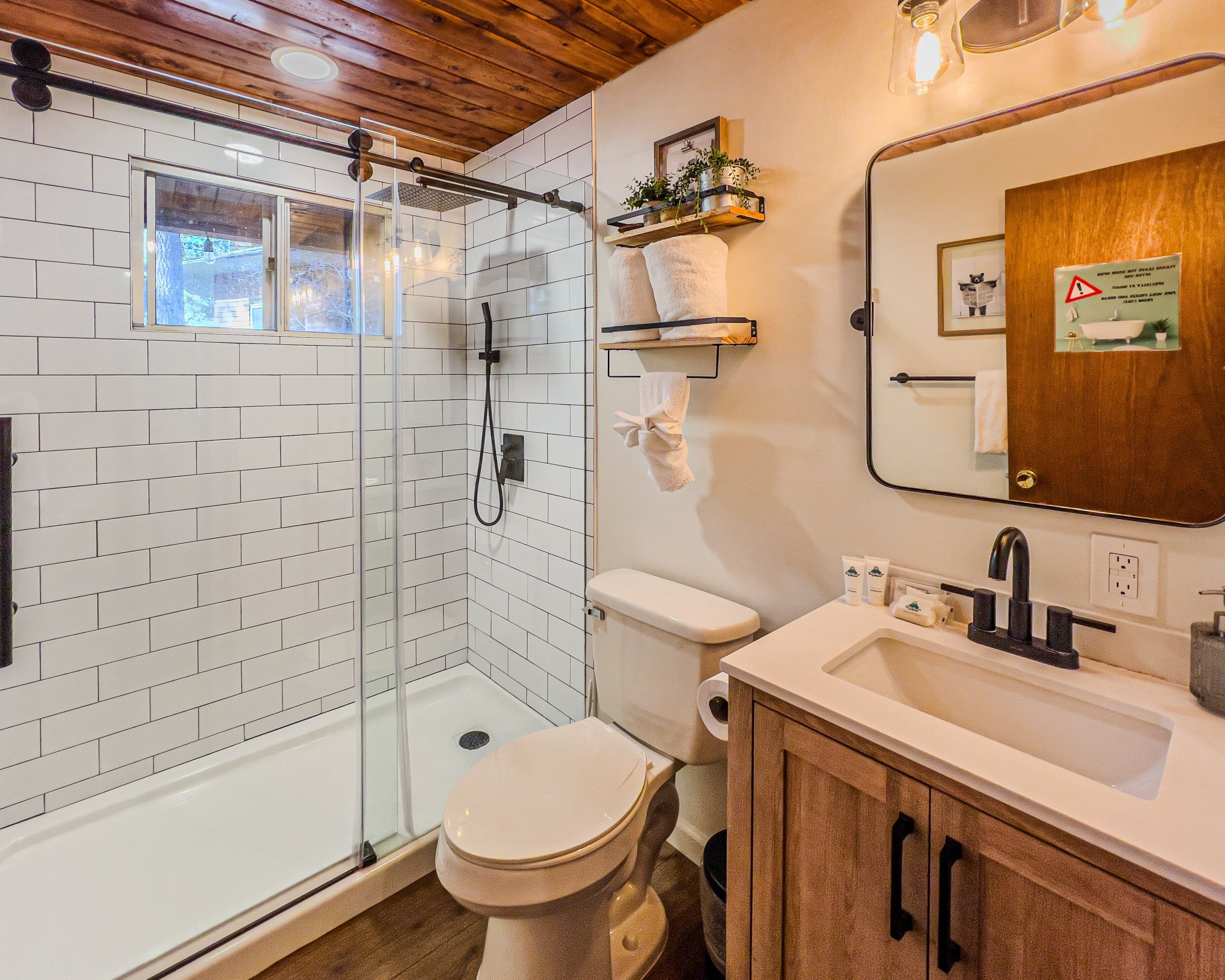 Un baño moderno con ducha envuelta en vidrio, inodoro, lavamanos con espejo y armarios de madera.