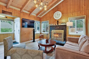 A cozy living room with wooden walls, a stone fireplace, a large clock, and a television. - Sweet Retreat Combo #2334 (Big Bear Lake)