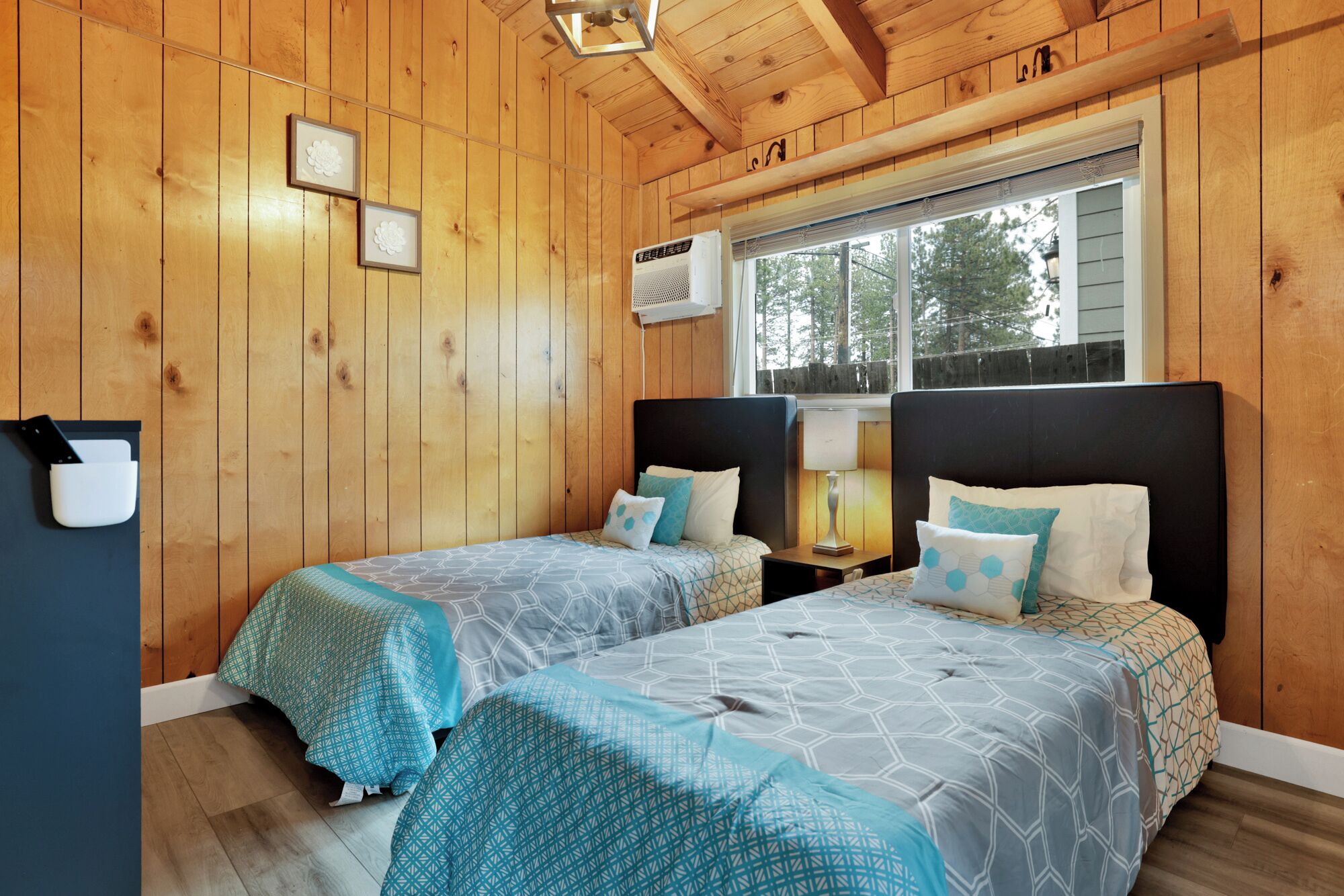A wooden cabin bedroom with two beds, a window, and a wall-mounted air conditioner.