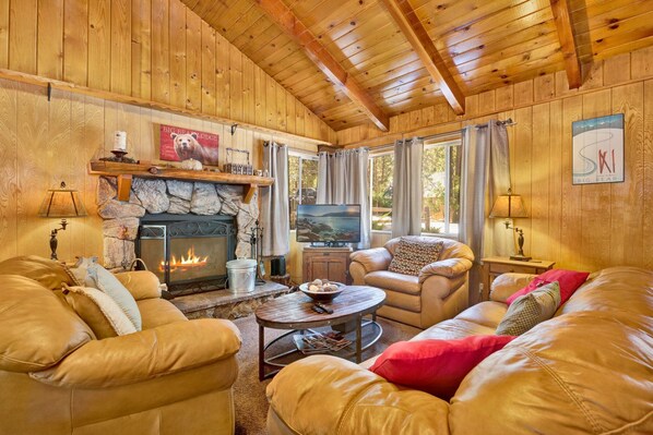 Ein gemütliches Blockhaus-Interieur mit Ledersofas, einem Kamin aus Stein, einem Fernseher und einem Steinsims.