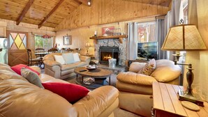 Un intérieur chaleureux de chalet en bois avec une cheminée en pierre, des canapés en cuir et un coin repas.