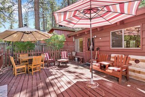 Eine Holzterrasse mit Gartenmöbeln, darunter Stühle und ein Tisch, unter gestreiften Sonnenschirmen.