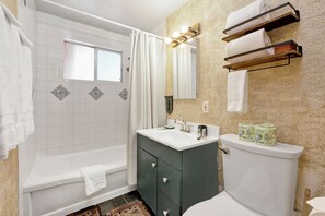 Ein Badezimmer mit einer Badewanne, einem Waschbecken und einer Toilette. Handtücher hängen an der Wand und ein Duschvorhang ist angebracht.