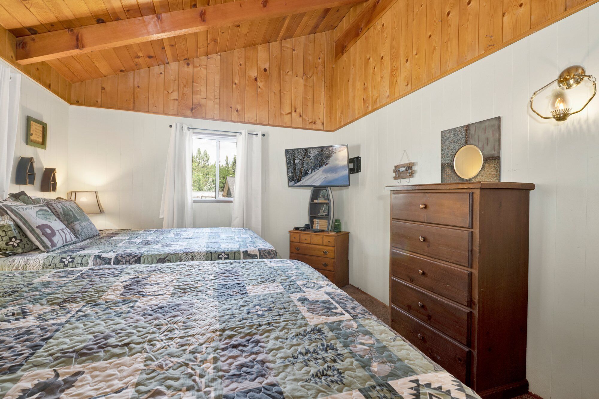 Un dormitorio con dos camas, un aparador de madera, un televisor y una ventana con cortinas.
