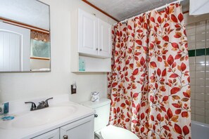 A bathroom with a white sink, mirror, and cabinet, a toilet, and a shower curtain with a leaf pattern.