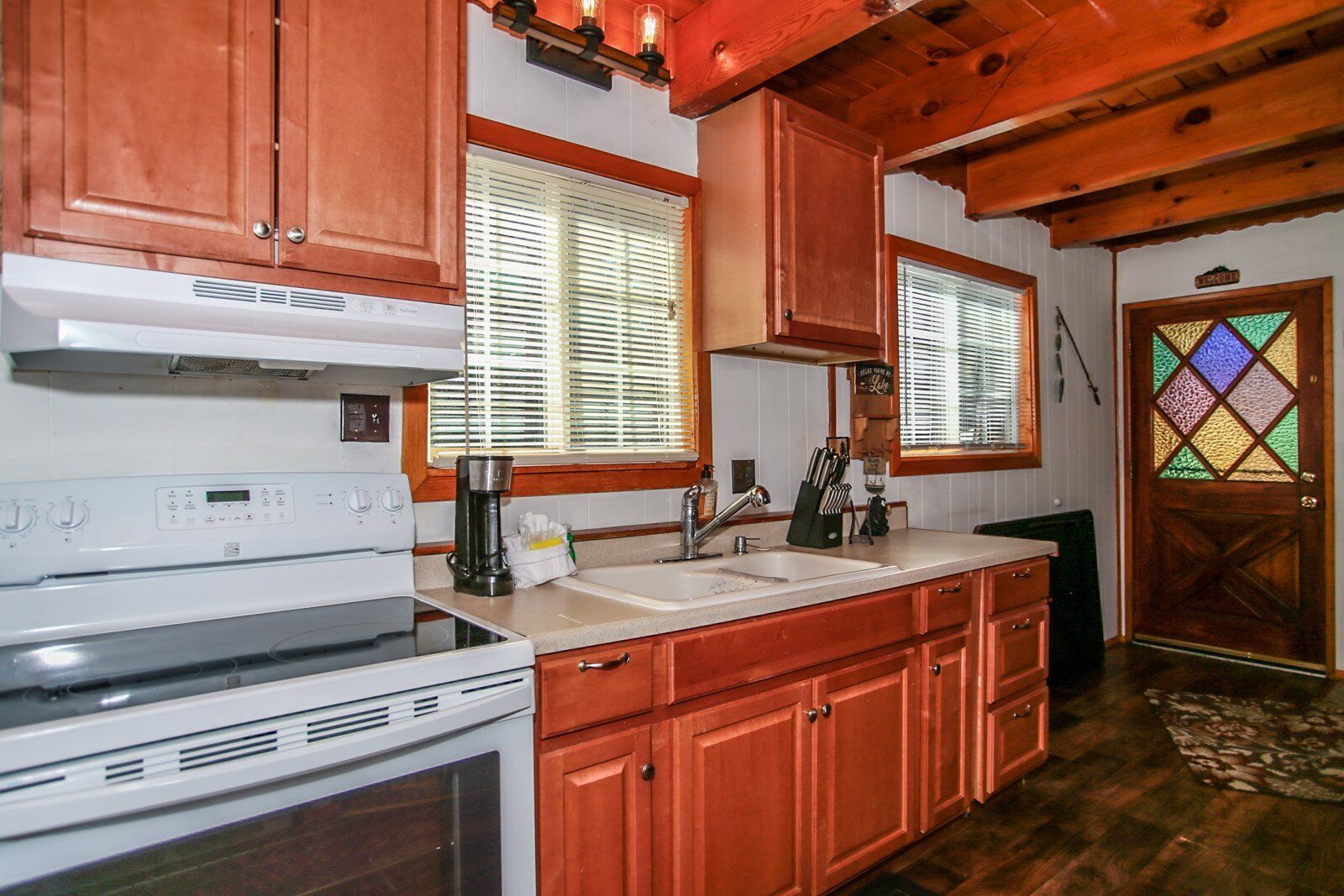 A kitchen with wooden cabinets, a stove, a sink, and a window with blinds.