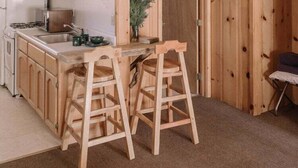 Interieur van een houten chalet met een keukenhoek, houten krukken en een 'WELCOME'-bord.