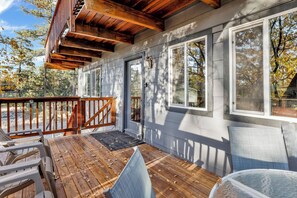 A covered deck with wooden railings, a seating area with chairs, and a view of the surrounding trees. - Chipmunk Treehouse #1983 (Big Bear Lake)
