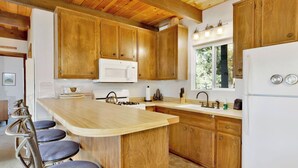 A kitchen with wooden cabinets, a white microwave, a sink, and a refrigerator. - Chipmunk Treehouse #1983 (Big Bear Lake)