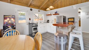 A kitchen with white cabinets, a stainless steel stove, wooden ceiling beams, and a small dining table with chairs.