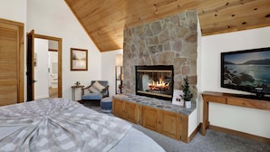 A bedroom with a stone fireplace, wooden ceiling, and a television on the wall. - Green Canoe Cabin #2293 (Big Bear Lake)