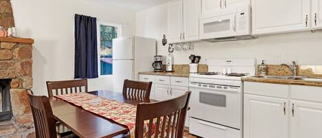 A compact kitchen with white cabinets, a gas stove, a microwave, and a refrigerator. There is a dining table with chairs and a rug on the floor.