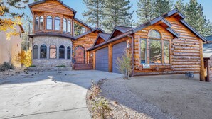 A log cabin with a stone foundation, multiple garage doors, and a driveway leading to a gravel area.