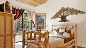 A bedroom with a rustic wooden bed frame, a large window with curtains, and a tree branch wall decoration.