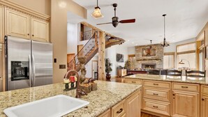A spacious kitchen with granite countertops, wooden cabinets, a stainless steel refrigerator, and a stone fireplace.