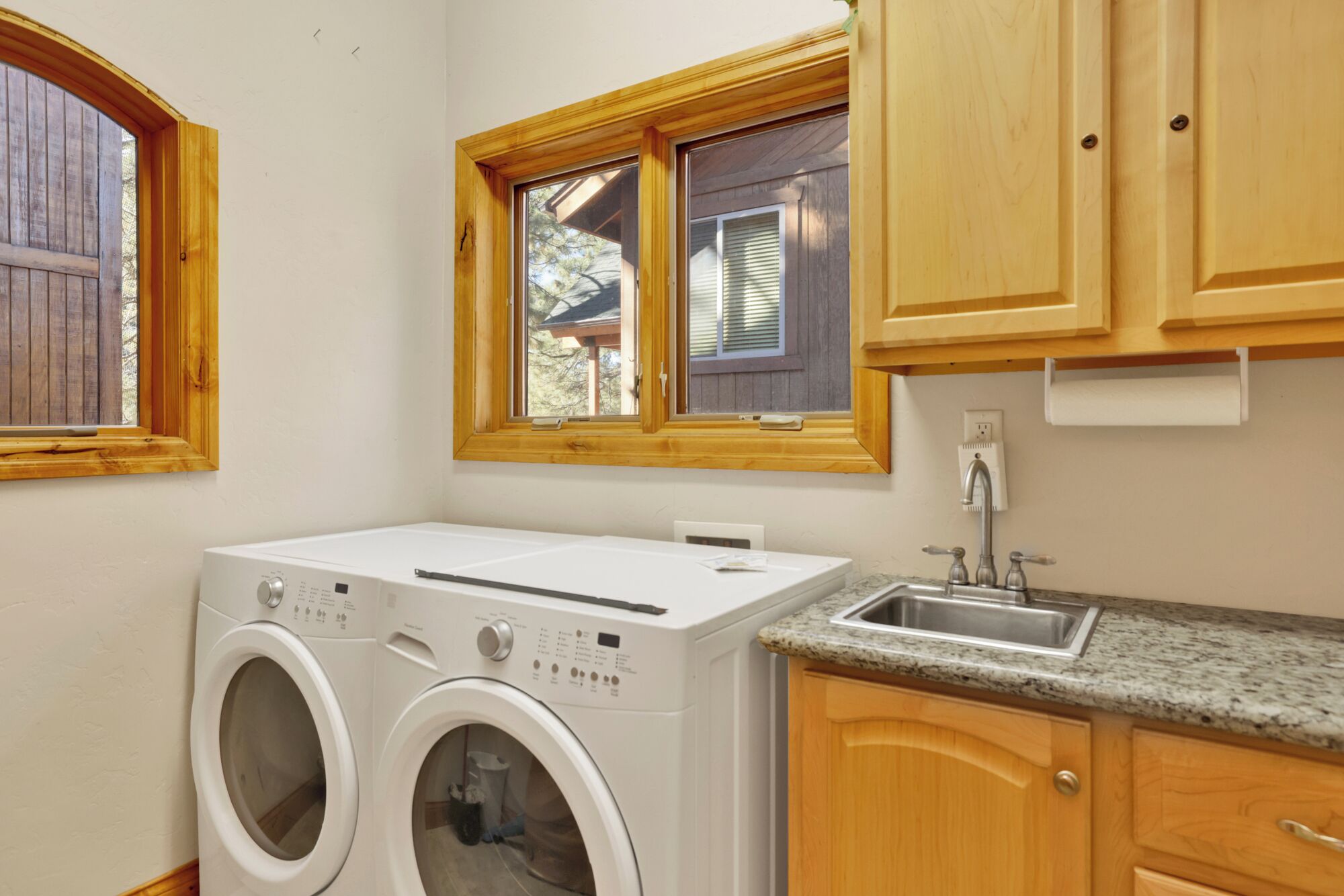 Un cuarto de lavandería con dos lavadoras, un lavabo, armarios de madera y una ventana con persianas.