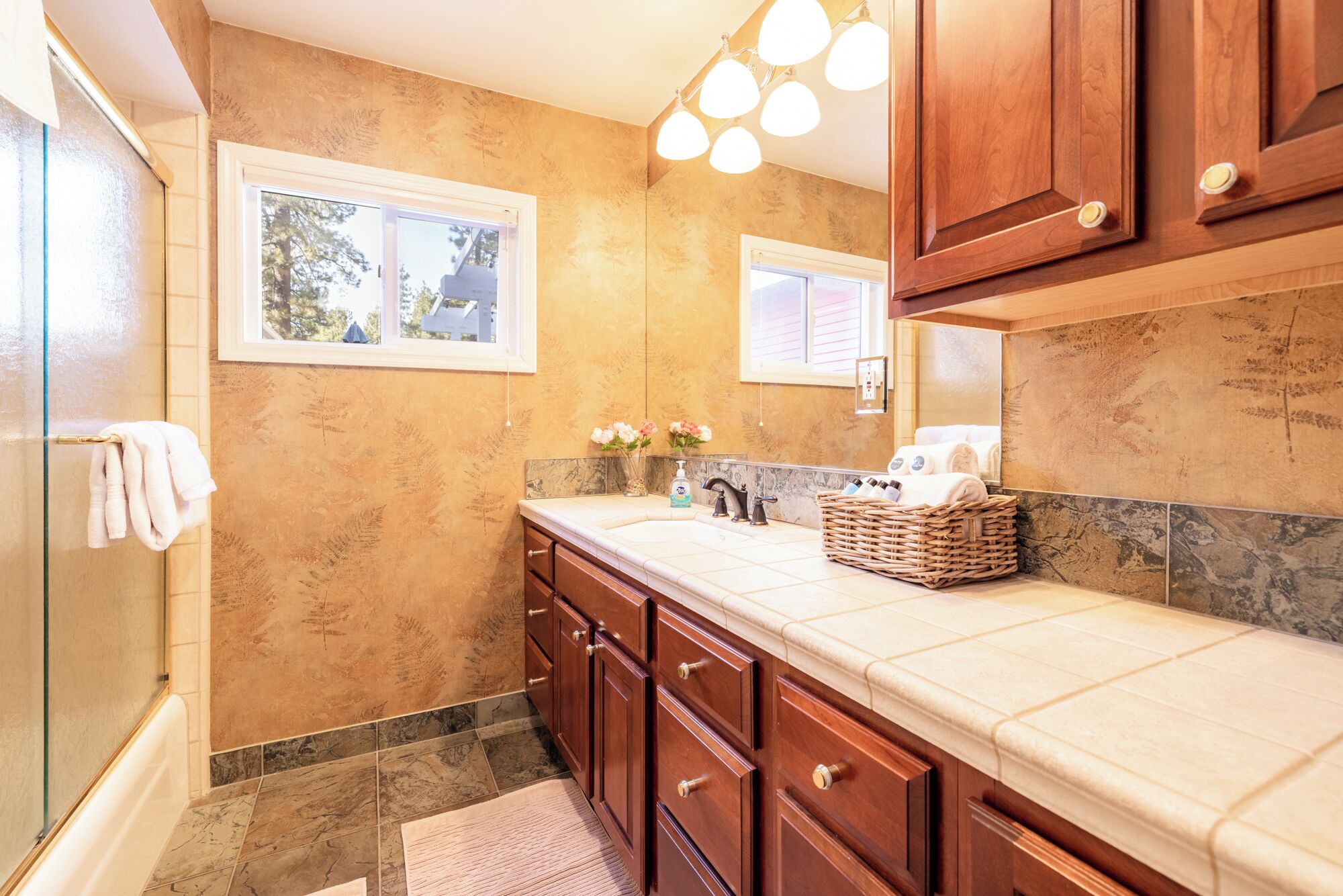 A bathroom with a large window, a sink with a mirror, and a wooden cabinet.