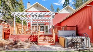 A red house with a covered patio, a hot tub, and a wooden deck.