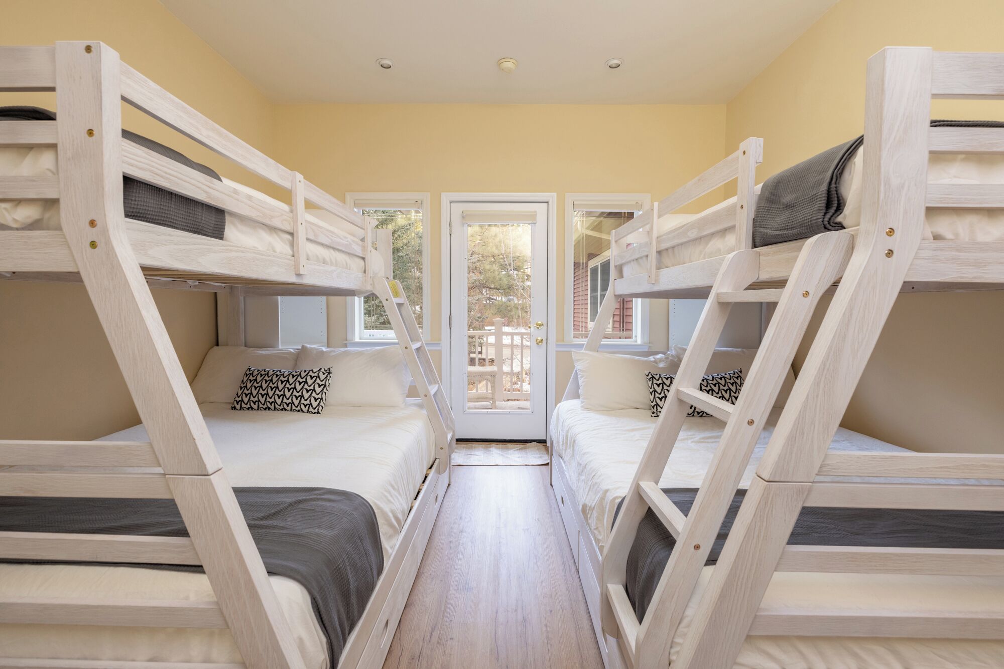 Een kamer met stapelbedden, een houten vloer en een deur naar buiten.