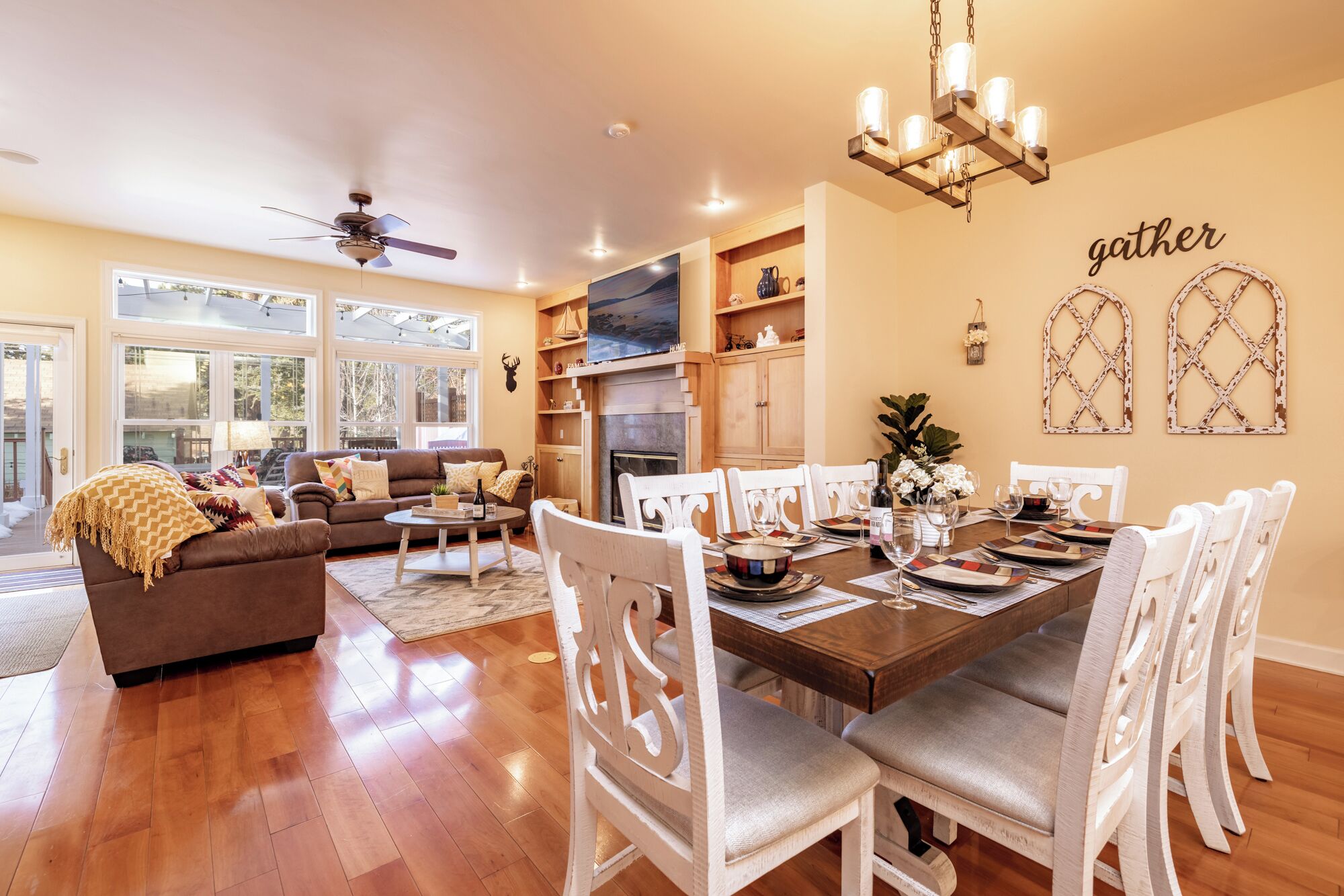 A spacious living room with a fireplace, a dining area with white chairs, and a kitchen with wooden cabinets.