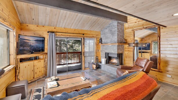 A cozy cabin interior with a fireplace, wooden walls, a television, and a balcony with a view of trees.