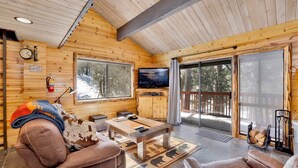 A cozy cabin interior with a wooden interior, a fireplace, a television, and a large sliding glass door leading to a deck.