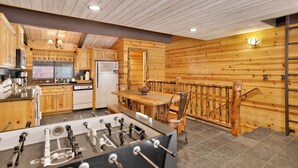 A cozy wooden cabin interior with a kitchen, dining area, and a foosball table.