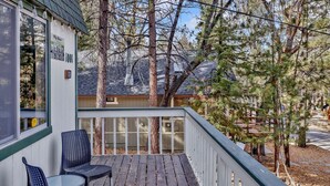 A wooden deck with two wicker chairs and a glass table, overlooking a residential area with trees and houses. - Pinewood INN #2093 (Big Bear City)