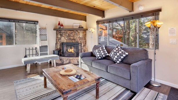 A cozy living room with a stone fireplace, a grey sofa, and a wooden coffee table. - Pinewood INN #2093 (Big Bear City)