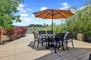 Une terrasse avec une table et des chaises, un grand parasol, et une vue sur un parc et des bâtiments en arrière-plan.