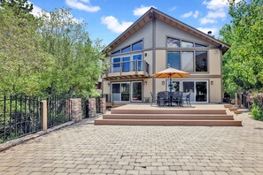 Une maison moderne à deux étages dotée d’un patio aménagé avec du mobilier d’extérieur et un grand parasol.