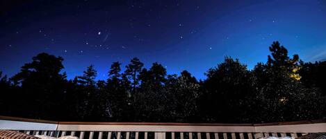 Cielo nocturno con estrellas visibles sobre un balcón con mobiliario de mimbre.