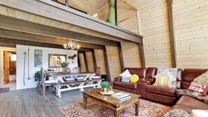 En rummelig loftstue med højt til loftet, træbjælker, en lædersofa i brunt, et træbord og et mønstret tæppe.