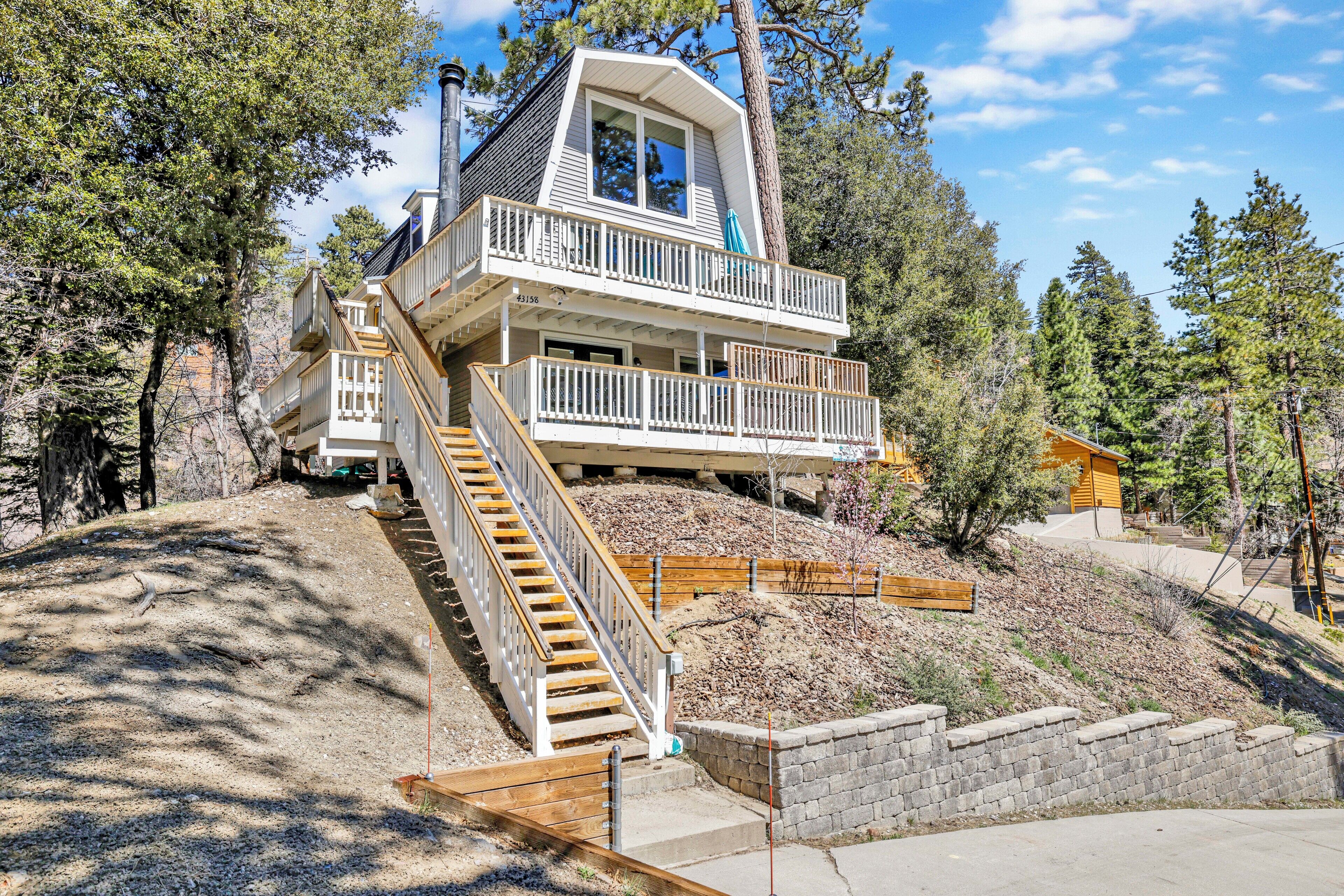 A two-story house with a balcony, a staircase leading to the upper floor, and a view of the surrounding forest.