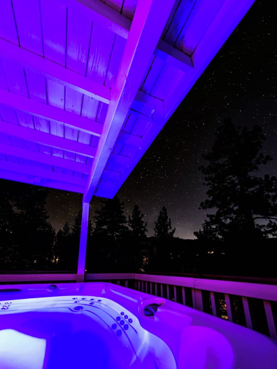 A hot tub under a starry night sky with a wooden deck and a railing.