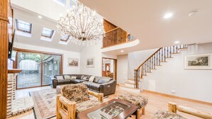 A spacious living room with a large sectional sofa, a coffee table, and a chandelier. There is a staircase leading to an upper level. - Bears Palace Chalet #2008 (Big Bear Lake)