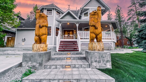 A large house with a porch, two bear statues, and a staircase leading to the front door. - Bears Palace Chalet #2008 (Big Bear Lake)