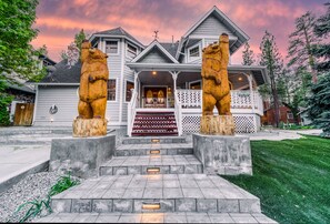 Une grande maison avec un porche, deux statues d’ours et un escalier menant à la porte d’entrée.