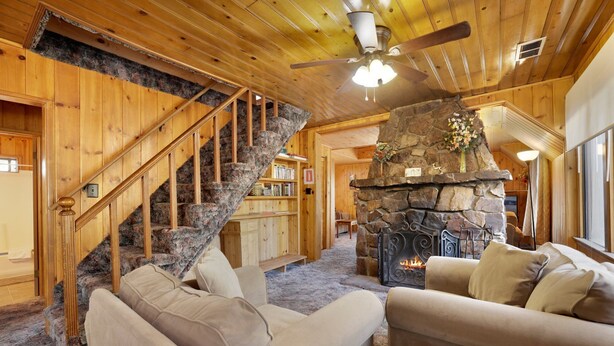 Un interior acogedor de cabaña con chimenea de piedra, escalera de madera y zona de estar confortable.