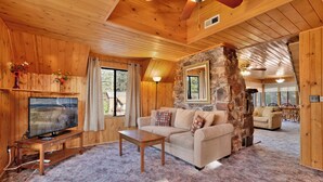 Un interior de cabaña acogedor con paredes de madera, un muro de acento de piedra, un televisor, un sofá y una zona de comedor.