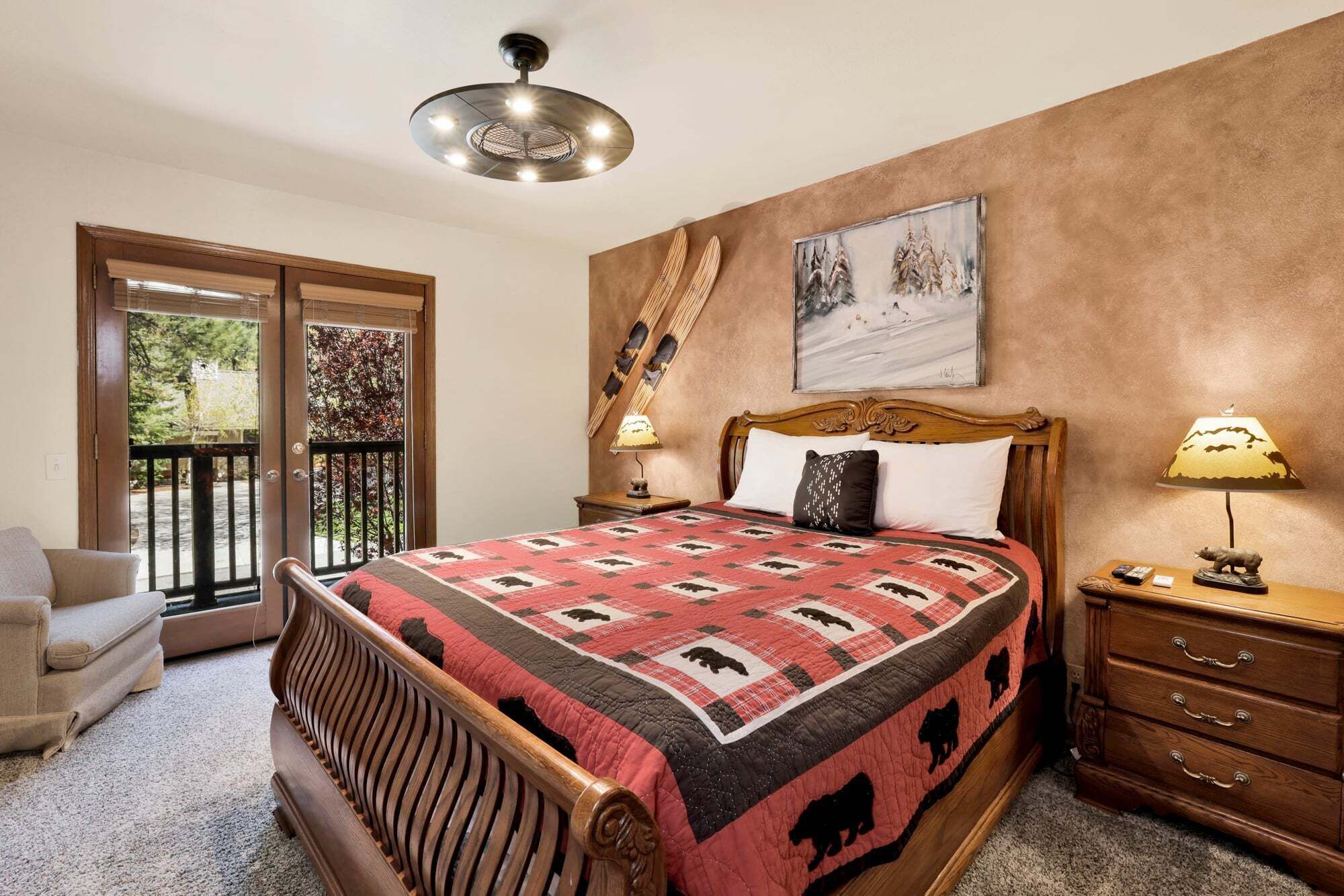 Een slaapkamer met een bed, een houten hoofdbord, een nachtkastje met een lamp, een dressoir, een schilderij aan de muur en een balkon met uitzicht.