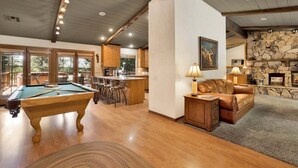 A pool table, bar area, and a fireplace in a well-lit room with wooden beams and stone accents. - Moose Manor #2012 (Big Bear Lake)