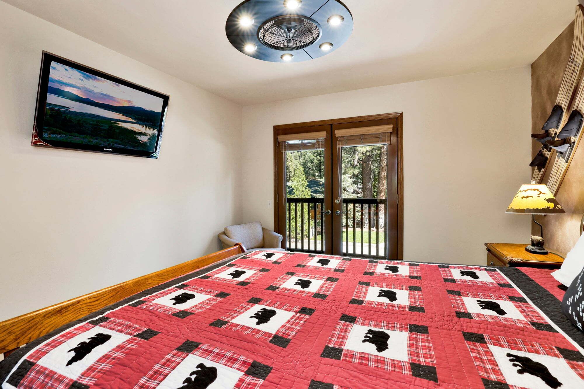 A bedroom with a bed, a television on the wall, a ceiling fan, and a view through the door.