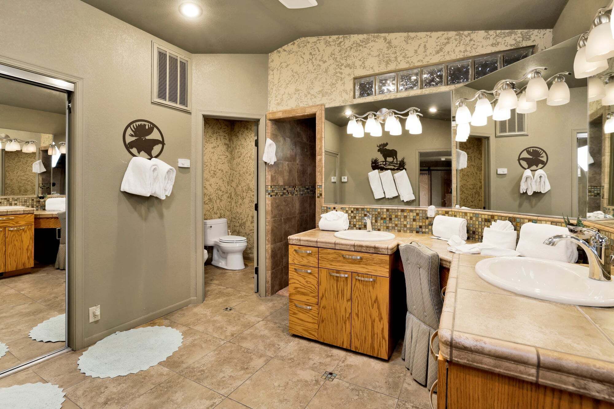 Une salle de bain avec un grand miroir, deux lavabos, des meubles en bois et des toilettes.
