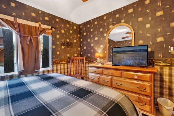 A bedroom with a plaid bedspread, a wooden dresser, a television, and a mirror on the wall.