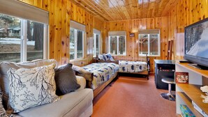 L’intérieur d’une cabane avec des murs en bois, deux lits avec une literie à motifs floraux, un canapé agrémenté d’un coussin à motifs, un téléviseur et une bibliothèque.