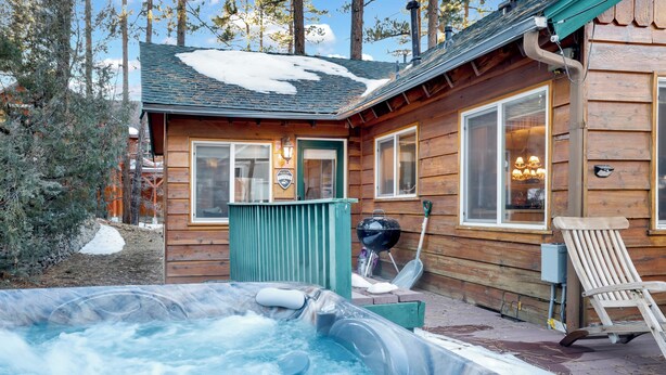 Une cabane en bois avec un jacuzzi, un barbecue et une chaise à l’extérieur.