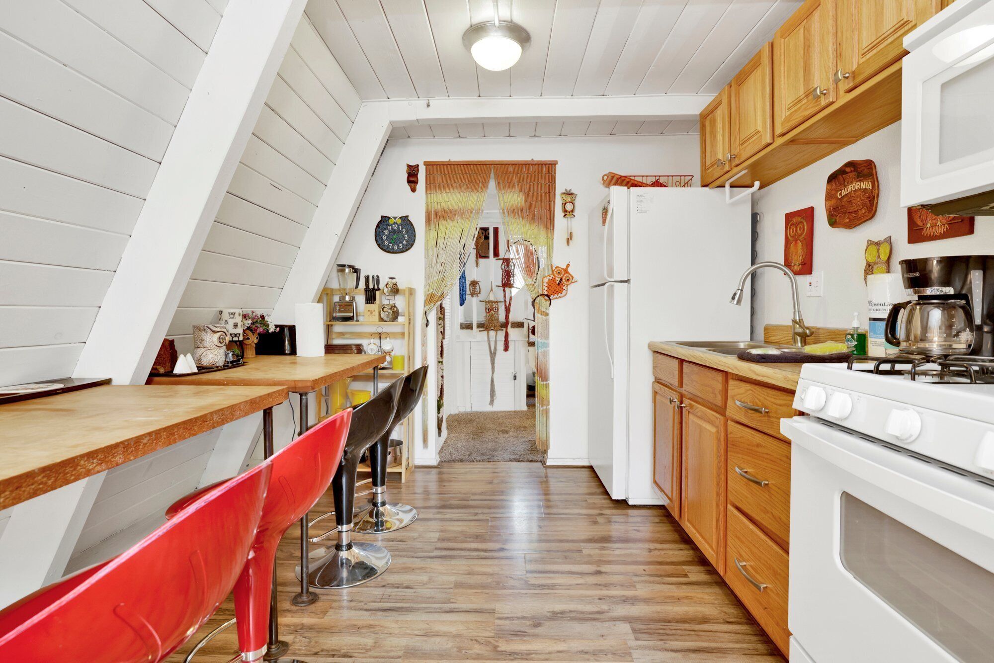 A kitchen with wooden cabinets, a stove, and a sink. There is a red chair and a wooden table.