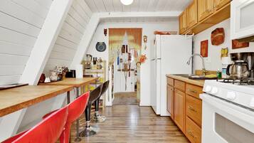 A kitchen with wooden cabinets, a stove, and a sink. There is a red chair and a wooden table.