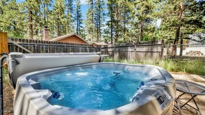 A hot tub in a backyard with a wooden deck, a metal chair, and a fence. - Sunrise Cottage #1800 (Big Bear City)